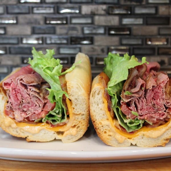 Two halves of a roast beef sandwich with lettuce, cheese, and sauce on a white plate.
