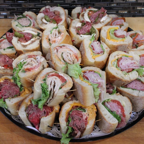 A large platter filled with various baguette sandwich halves, each secured with a toothpick.