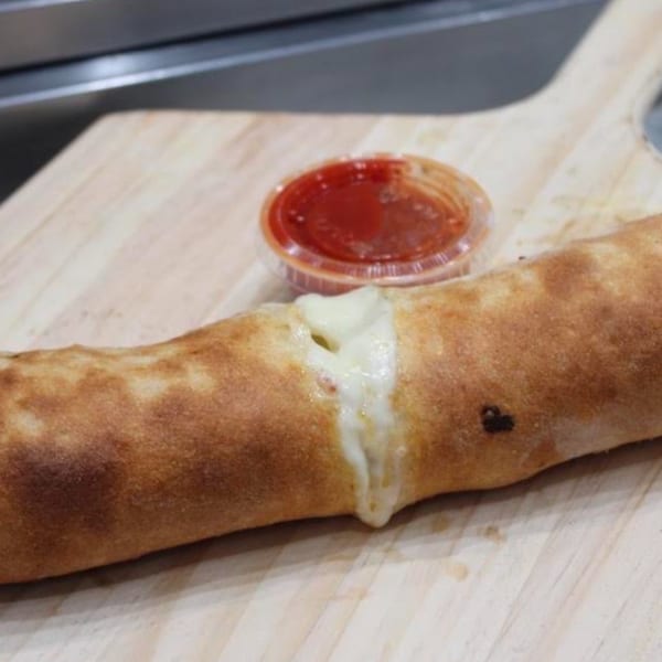 Golden-brown calzone with melted cheese oozing out, served with a side of marinara sauce on a wooden peel.