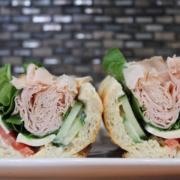 Two halves of a turkey sandwich on a white plate, filled with spinach, tomatoes, and cheese.