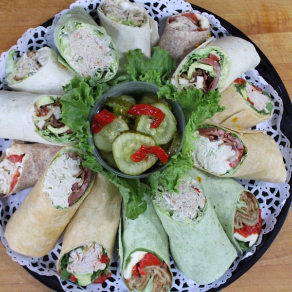 A platter of assorted wraps, including chicken salad, turkey, and tuna, with a side of pickles.