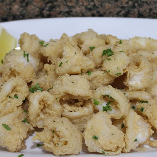 Crispy fried calamari rings with fresh parsley and lemon wedges on a white plate.