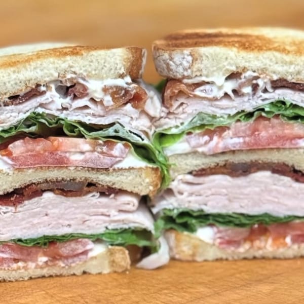 Two halves of a stacked club sandwich with turkey, bacon, lettuce, tomato, and mayonnaise.