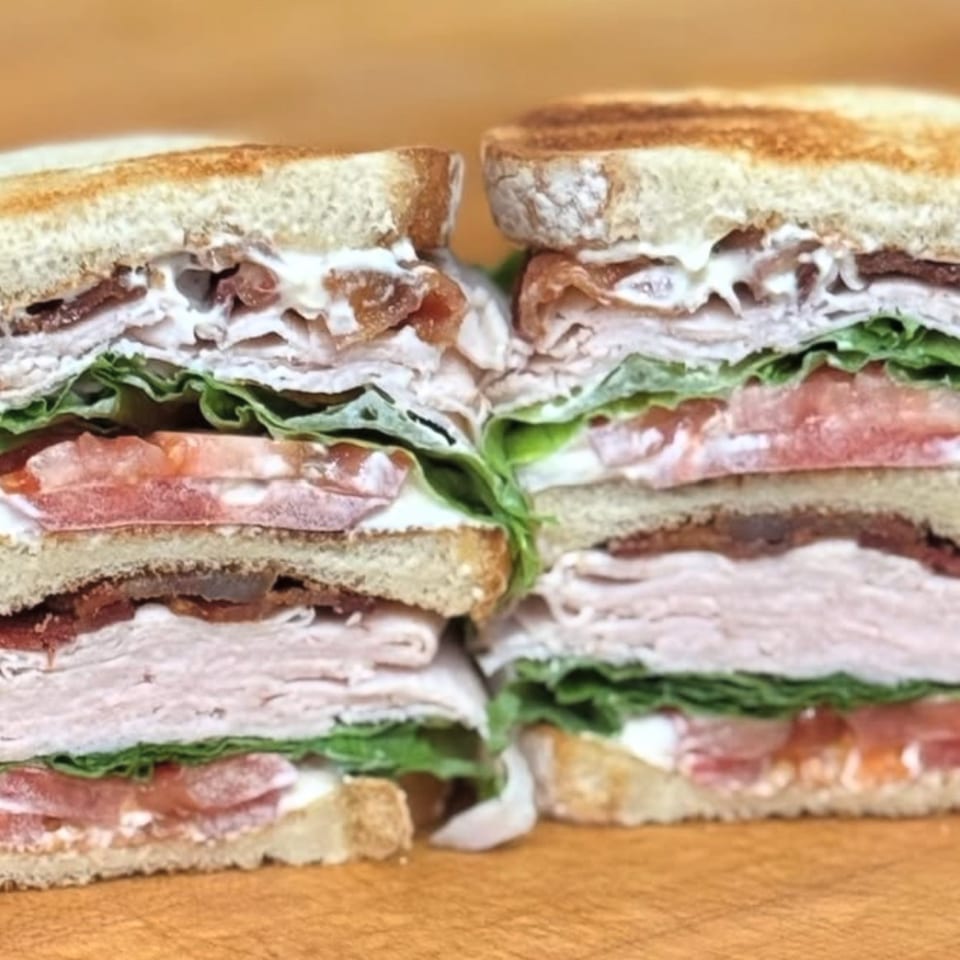 Two halves of a stacked club sandwich with turkey, bacon, lettuce, tomato, and mayonnaise.