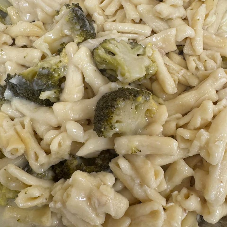Creamy pasta with broccoli florets, served in a foil container.
