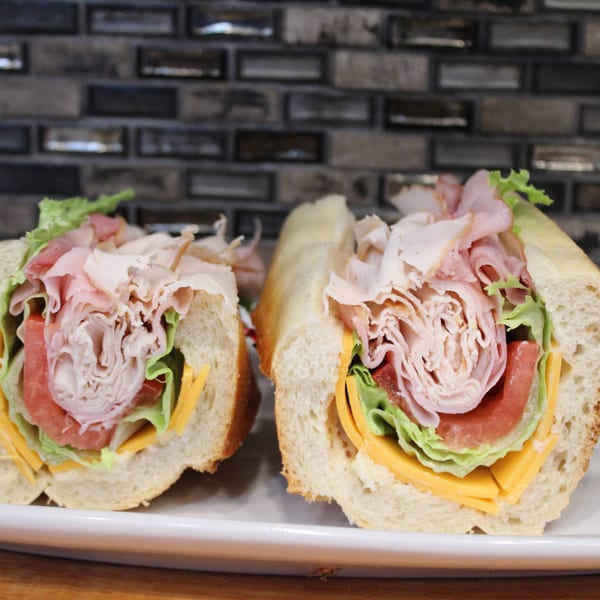 Two halves of a deli sandwich filled with turkey, ham, cheese, lettuce, and tomato.