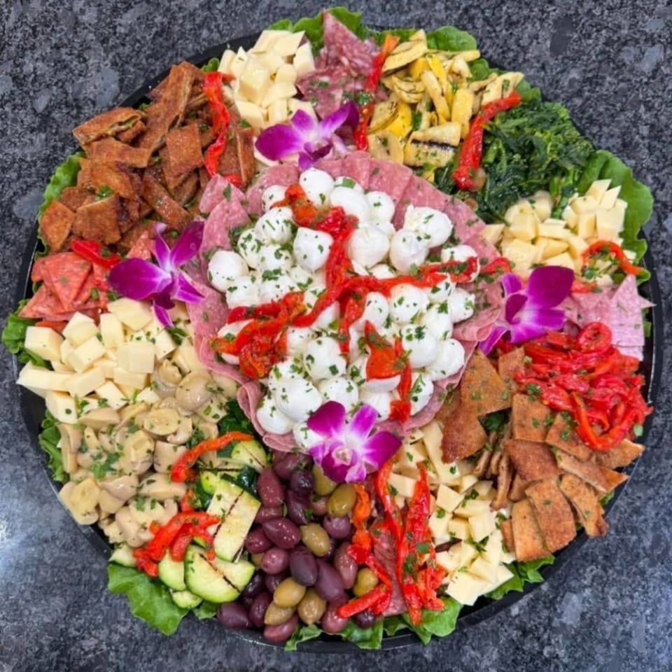 A large charcuterie board filled with meats, cheeses, olives, vegetables, and mozzarella balls.
