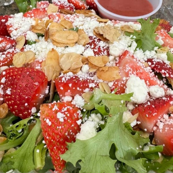 Strawberry salad with mixed greens, sliced almonds, feta, and strawberry vinaigrette on the side.