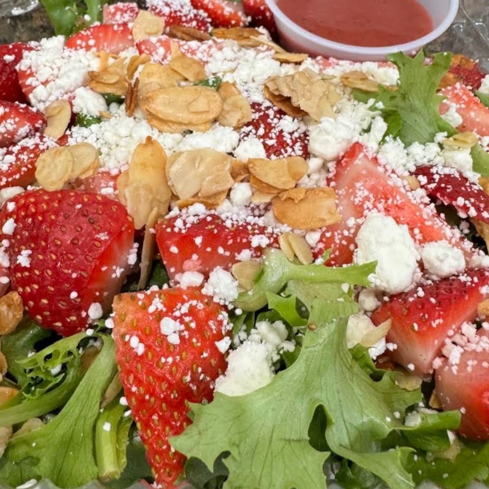 Strawberry salad with mixed greens, sliced almonds, feta, and strawberry vinaigrette on the side.