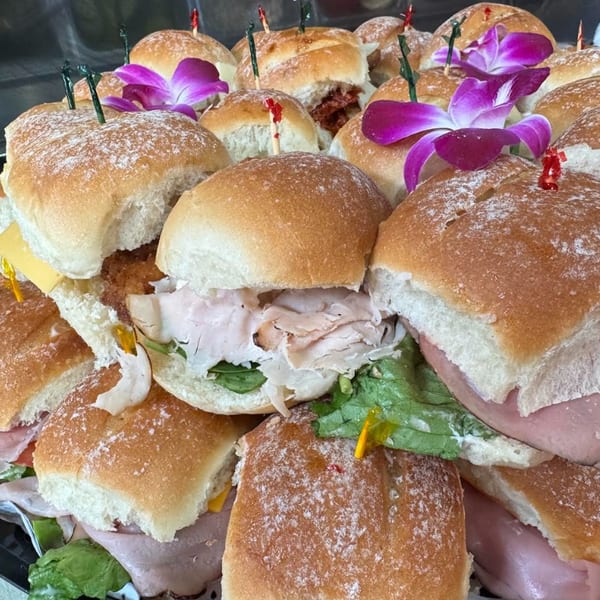 A platter of various mini sandwiches, some garnished with purple orchids, on a dark tray.
