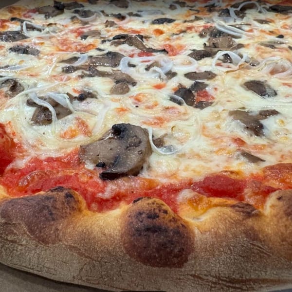 Brick oven pizza topped with mushrooms, onions, and melted mozzarella with a charred crust.