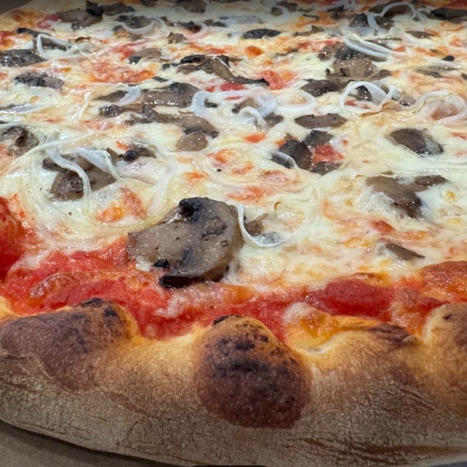Brick oven pizza topped with mushrooms, onions, and melted mozzarella with a charred crust.