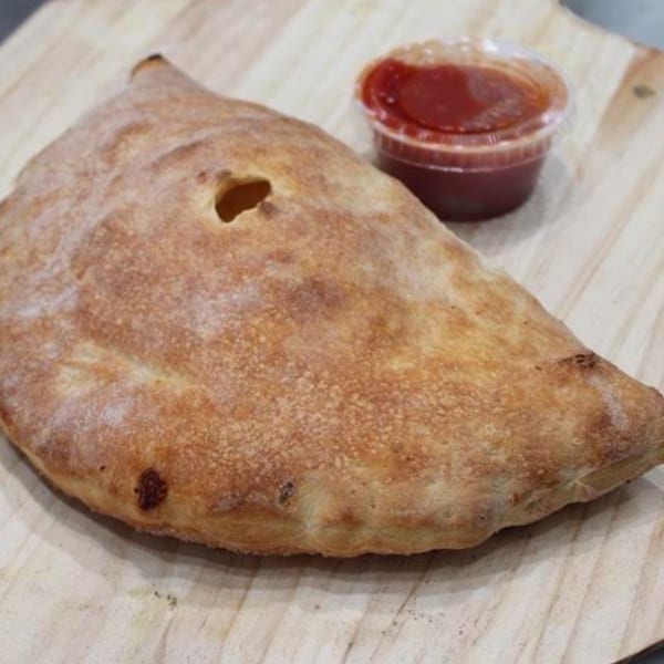 Golden-brown calzone with a small vent hole, served with a side of red dipping sauce.